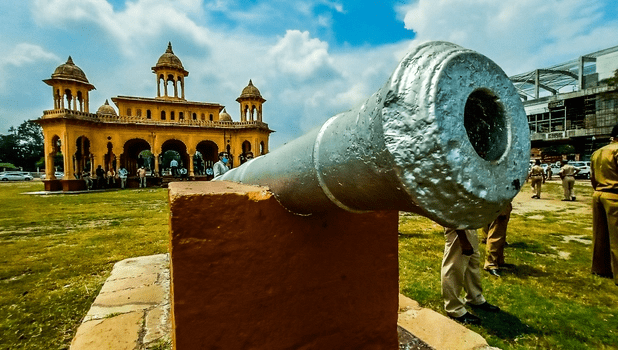 A beautifully restored Kasturchand Park bandstand glowing under soft evening lights, surrounded by lush greenery and visitors enjoying the space.